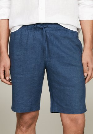 Mørkeblå linnedshorts med elastisk talje og snor. Skjorten har korte ærmer, krave og knaplukning foran.
