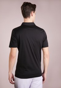 Svart polo skjorte laget av glatt materiale, med klassisk krage og korte ermer, vist fra bak. Enkel og ren design.