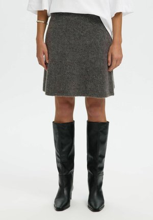 Jupe grise en laine avec une texture subtile et une coupe en A, associée à des bottes hautes en cuir noir avec un bout carré et une finition lisse.