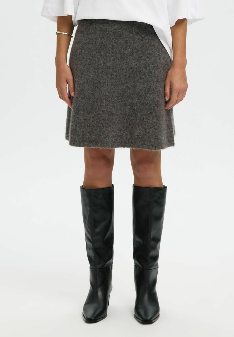Siva vunena suknja s suptilnom teksturom i A-linijom, uparena s crnim kožnim čizmama do koljena sa kvadratnim vrhom i glatkom završnom obradom.