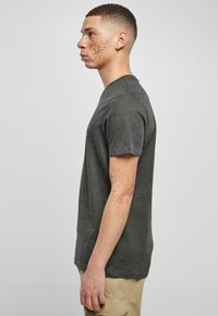 T-shirt grigio antracite a girocollo con maniche corte e una vestibilità rilassata, realizzato in tessuto morbido. Modello mostrato di profilo.