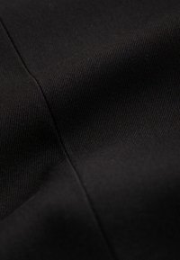 Tissu noir à texture lisse, présentant un motif tissé serré. Il présente un léger éclat et des lignes de couture visibles.