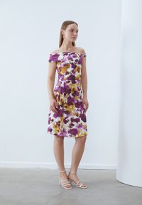 Blumenkleid mit schulterfreiem Design, lebendigen lila und gelben Mustern auf weißem Hintergrund und einer taillierten Taille mit plissiertem Rock.
