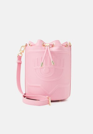 Różowa skórzana torba typu bucket z regulowanym paskiem, złotym metalowym okuciem, zamknięciem na sznurek i tłoczonym stylizowanym wzorem oka na przedzie.