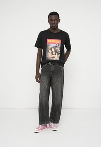 Čierne tričko s grafikou "PULP FICTION", kombinované s voľnými sivými džínsami s zaoblenými švami a ružovými teniskami s bielymi podrážkami.