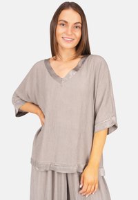 Lockere graue Bluse mit V-Ausschnitt, kurzen Ärmeln und Satinakzenten. Die Textur ist leicht zerknittert, was visuelles Interesse verleiht.