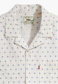 Biała koszula z krótkim rękawem z niebieskim wzorem kwiatowym, luźnym kołnierzykiem, przednią kieszenią i metką z logo Levi's. Teksturowana tkanina.
