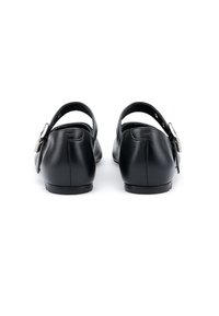 Para czarnych skórzanych butów bez obcasa typu slingback z srebrnymi klamrami, przedstawionych z tyłu na białym tle.