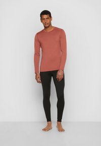 Long-sleeve, rust-colored shirt paired with black leggings. Both garments are fitted, made from a smooth fabric, and feature minimal design details.