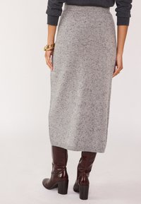 Jupe midi en tricot gris avec une finition texturée et de subtils éclats, associée à des bottes en cuir bordeaux montantes avec des talons épais.