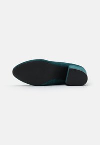 Teal Damen-Loafer mit schwarzer, strukturiertem Gummisohle und niedrigem Blockabsatz, von unten auf weißem Hintergrund gezeigt.
