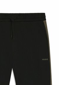 Sorte joggers med elastisk talje, pyntet med en grøn sidebånd og et logo, der siger "HUGO" nederst til venstre.