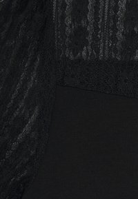 Top negro con una superposicón de encaje texturado con patrones florales, combinado con una tela suave debajo, ambos en un color negro sólido.