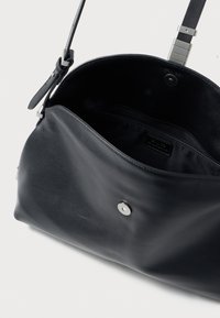 Schwarze Lederhandtasche mit glatter Oberfläche, ausgestattet mit einem silbernen Druckverschluss und einem Schulterriemen. Innenraum sichtbar, zeigt das Futter.