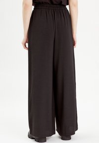 Pantalon noir à jambes larges avec une ceinture élastique, fabriqué en tissu doux, présentant une coupe ample et un détail de texture minimal.
