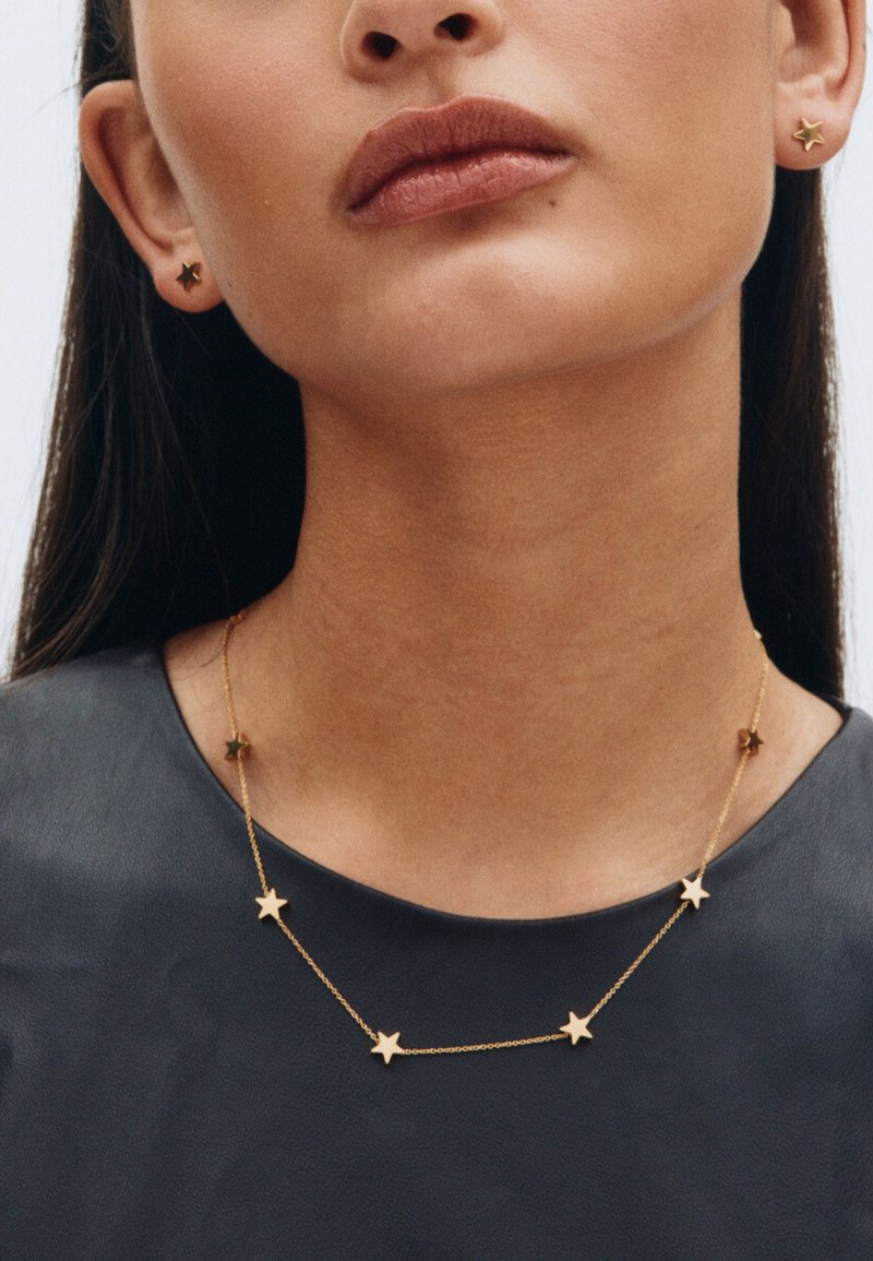 Ogrlica i naušnice u obliku zvijezda zlatne boje. Ogrlica ima pet zvijezda na nježnoj lancu, a naušnice su male kopče u obliku zvijezda.