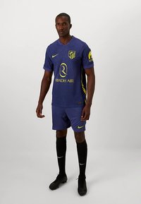 Lilla fotballtrøye med vertikal ribbestruktur, gule detaljer og logo. Kombinert med matchende shorts og svarte sokker. Svarte fotballsko.