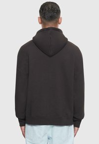 Sweatshirt noir à capuche avec une coupe décontractée, poignets et ourlet côtelés, et une texture douce. Comprend une couture centrale au dos.