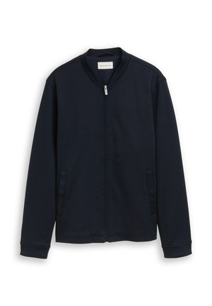 Chaqueta azul marino con cremallera, mangas largas, cuello alto y dos bolsillos laterales, mostrada sobre un fondo blanco.