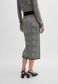 Personne portant une jupe écossaise taille haute arrivant au genou avec une ceinture noire et des chaussures à talons noires à bride arrière, se tenant contre un fond uni.