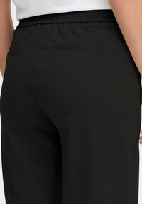 Black jogger pants featuring a simple design, elastic waistband, and two back pockets. Soft texture with a smooth, matte finish.