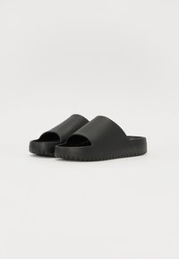 Musthave mustad släbisaapad avatud varvastega ja laia rihmaga, millel on tekstureeritud tald haardeks. Sile viimistlus ilma lisakaunistusteta.