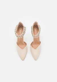Scarpe con tacco alto beige con design a punta e decorazioni di strass attorno alla caviglia. Tessuto liscio.