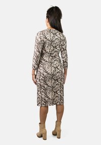 Vestido de patrón marrón y crema con mangas de tres cuartos, cintura ajustada, dobladillo hasta la rodilla, combinado con botines beige.