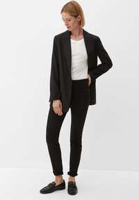 Blazer noir sur un t-shirt blanc, associé à un pantalon slim noir et des mocassins noirs. Tissu lisse et design ajusté avec des manches retroussées.
