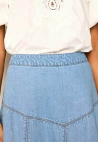 Jupe en jean bleu clair avec une taille �élastique, présentant des coutures visibles et une surface légèrement texturée, montrée au niveau de la taille.