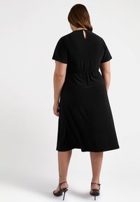 Zwarte midi-jurk van een zachte stof, met korte mouwen en een keyhole-detail op de rug. Het ontwerp heeft een elastische taille voor een mooie pasvorm.