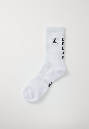 Bela rebrasta crew nogavica z črnim logotipom Jumpman in besedilom "JORDAN" na strani, leži ravno na belem ozadju.