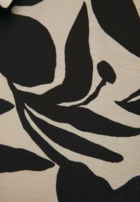 Sort blomsterdesign på et lyst beige stof med glat tekstur, der viser dristige blade og stilke i kontrast.