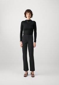 Black long-sleeve top paired with high-waisted black trousers, featuring a sleek fit and smooth texture. Black strappy heeled sandals complete the look.