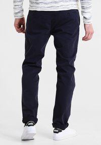 Granatowe bawełniane spodnie o slim fit, z przednimi kieszeniami i gładką fakturą. Noszone z białymi sneakersami z logo Nike.