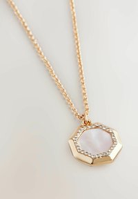 Guldtonad halsband med en oktagonal medaljong som har en ljusrosa stencenter omgiven av klara kristaller längs kanten.