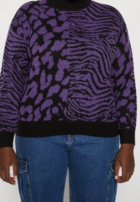 Schwarzer und lila gemusterter Strickpullover mit hohem Kragen, der eine Mischung aus Tiermotiven zeigt. Der untere Saum ist gerippt, und die Ärmel haben eine entspannte Passform.