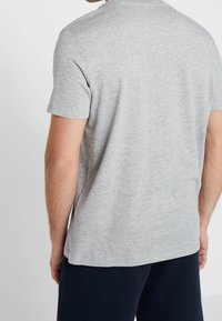 T-shirt z krótkim rękawem i okrągłym dekoltem, wykonany z jasnoszarej bawełny. Gładka faktura, luźny krój, prosty dół, bez widocznych ozdób.