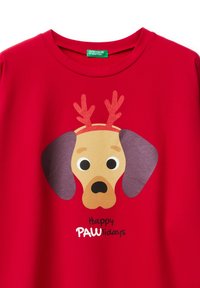 Czerwona koszulka z nadrukiem kreskówkowego psa w reniferowych porożach. Napis mówi „Wesołych Łapkowych Świąt”. Miękki bawełniany materiał z nadrukiem.