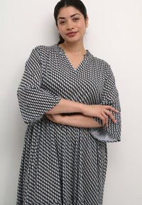 Haljina s uzorkom u crno-bijeloj boji, s v-izrezom, rukavima do tri četvrtine i lepršavim dizajnom. Izrađena od lagane tkanine s geometrijskim printom.