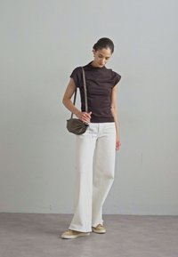 Schwarzes enges Oberteil mit kurzen Ärmeln, weiße weite Hosen und beige Sneakers. Trägt eine kleine olivgrüne Umhängetasche.