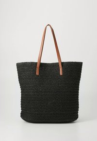 Sac fourre-tout tissé noir avec deux bretelles d'épaule en cuir marron, debout sur un fond gris clair uni.