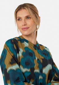 Halenka s dlouhým rukávem v barevném, abstraktním vzoru s tyrkysovými, hnědými a černými tóny. Dokončena kulatým výstřihem a zapínáním na knoflíky.