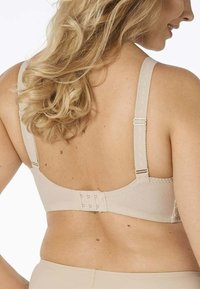 Soutien-gorge beige con spalline regolabili, chiusura con gancio e occhiello, materiale liscio e design della parte posteriore senza cuciture.