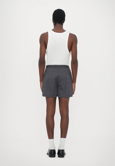 Shorts de bain à pois noirs et blancs avec une taille élastique, associés à un débardeur blanc, vus de dos.