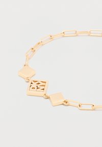 Aranyszínű lánc karkötő három négyzet alakú medállal, az egyik medálon kivágott "DKNY" betűk fehér háttéren.