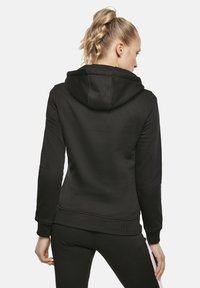 Sudadera con capucha negra, fabricada en un tejido suave, con puños acanalados y un bolsillo tipo canguro. El diseño presenta una silueta limpia y minimalista.