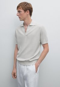 Lysgrå kortærmet polo skjorte med ribbet tekstur, der har en lav V-udskæring og en figursyet design, parret med hvide linnedbukser.