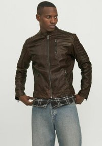 Braune Leder-Motorradjacke mit gerippten Schulterakzenten, Reißverschlusstaschen und Stehkragen, über einem karierten Hemd getragen.