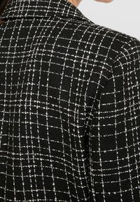 Black and white checked fabric with a textured finish. The design features a subtle grid pattern and a classic collar detail.